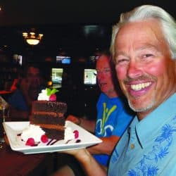 A man smiles holding a piece of chocolate cake