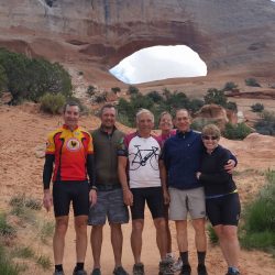 A group of bikers in front of a natural arch in Moab, Utah