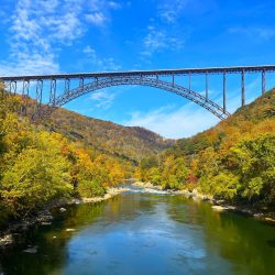 The landmark New River Gorge Bridge as seen from the river, rising from the fall foliage