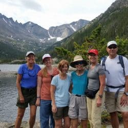 A group of hikers pose in front of a pond in the Rocky Mountains