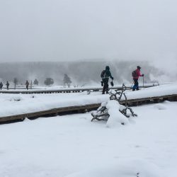 2 people hiking through Biscuit Basin boardwalk on snowshoes in Yellowstone National Park